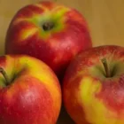 Drei rot-gelbe Äpfel liegen auf einer Holzfläche.